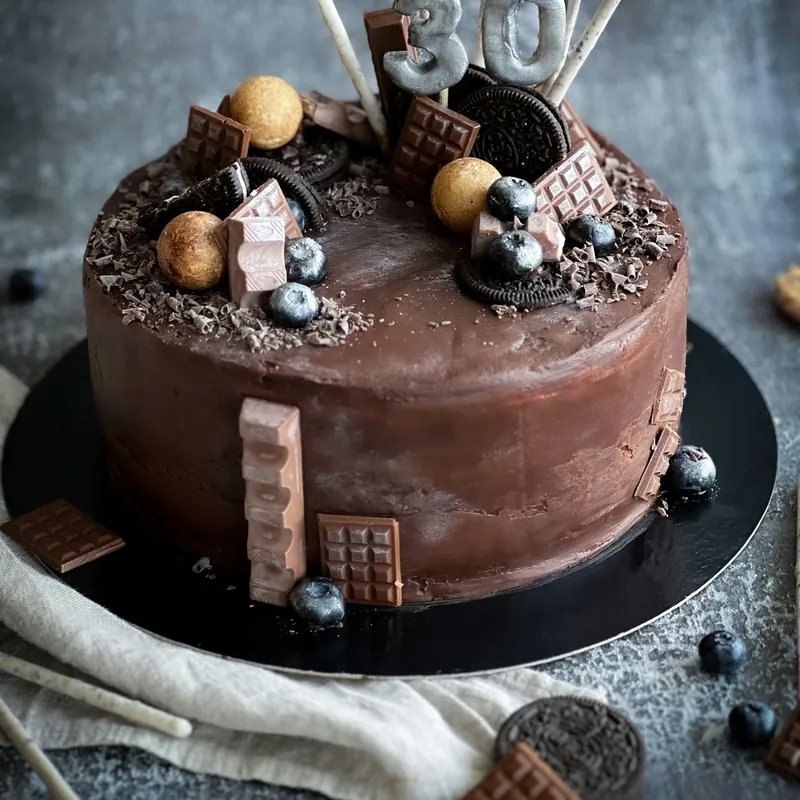 A chocolate drip cake decorated with cookies and chocolate pieces