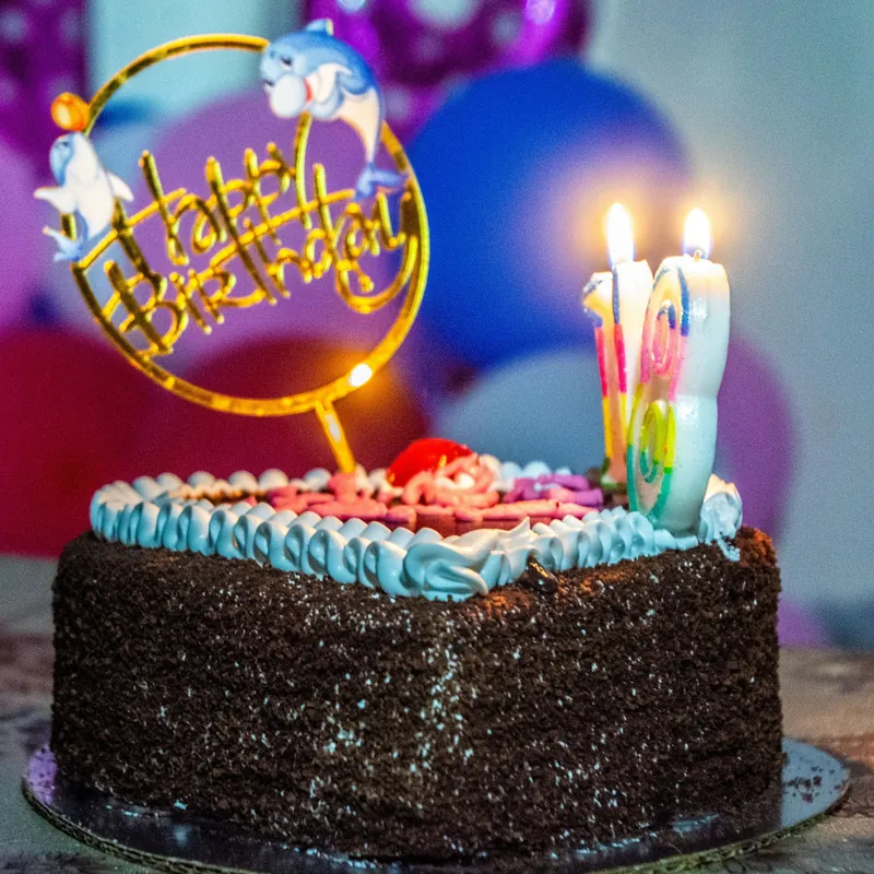 A chocolate birthday cake with lit candles and a Happy Birthday topper