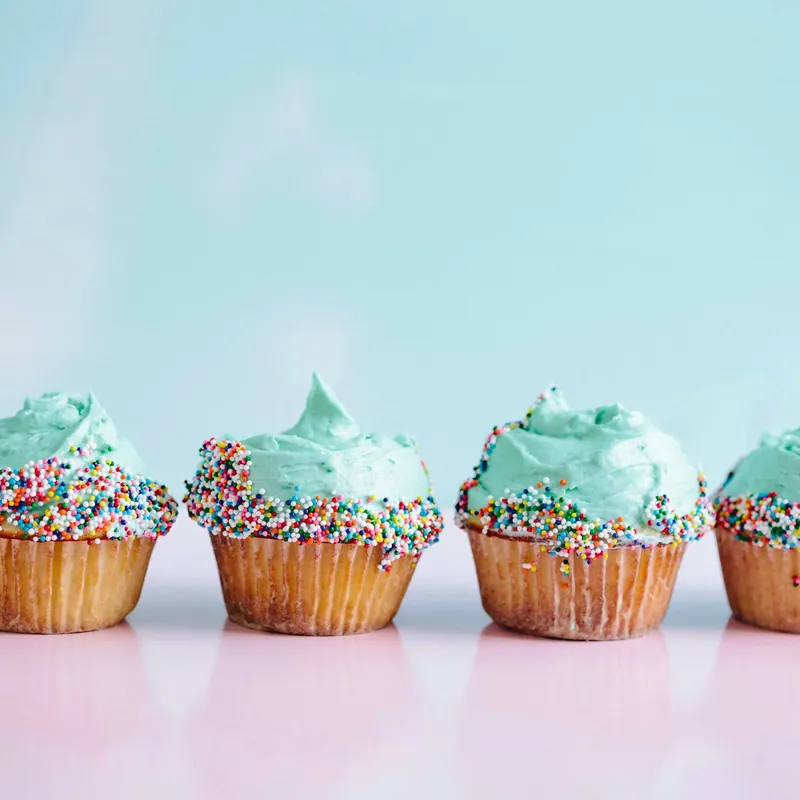 A row of cupcakes with teal frosting and rainbow sprinkles