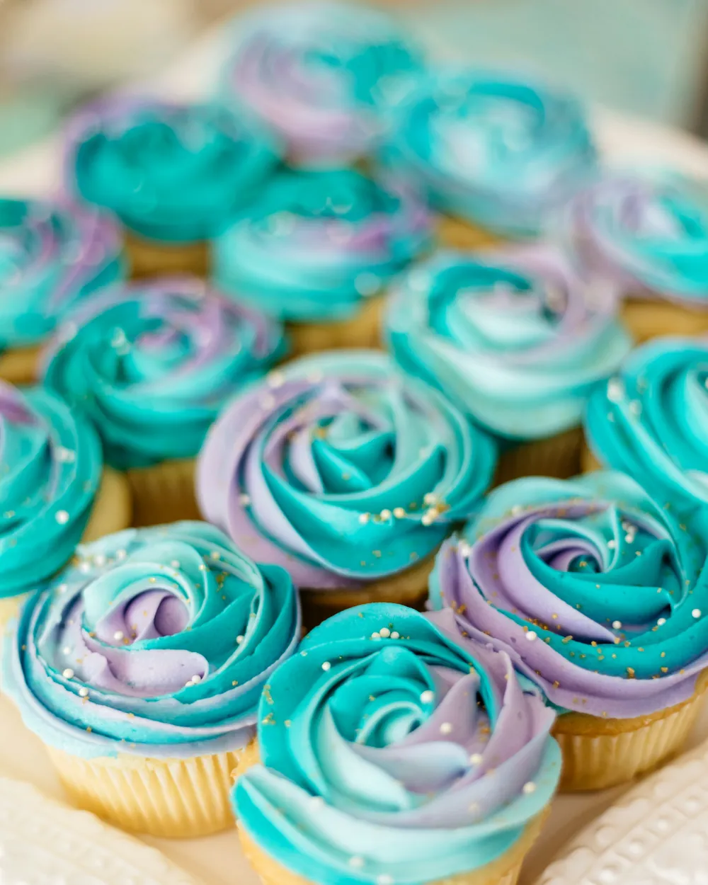 A tray of cupcakes piped with teal and lilac buttercream rosettes