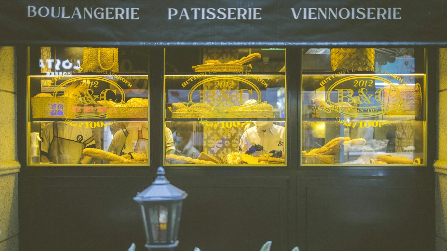 A lit bakery shopfront window with pastries on display