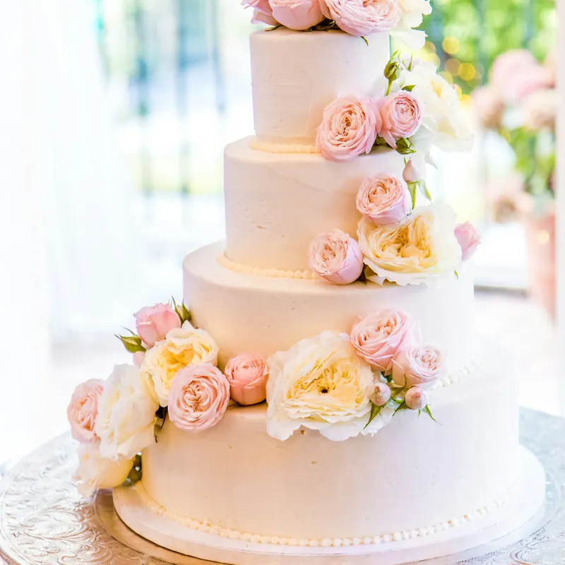 A four-tier white wedding cake dressed with blush roses