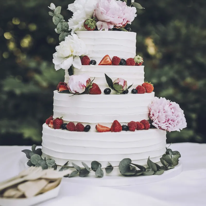 A three-tier wedding cake with fresh berries and peonies